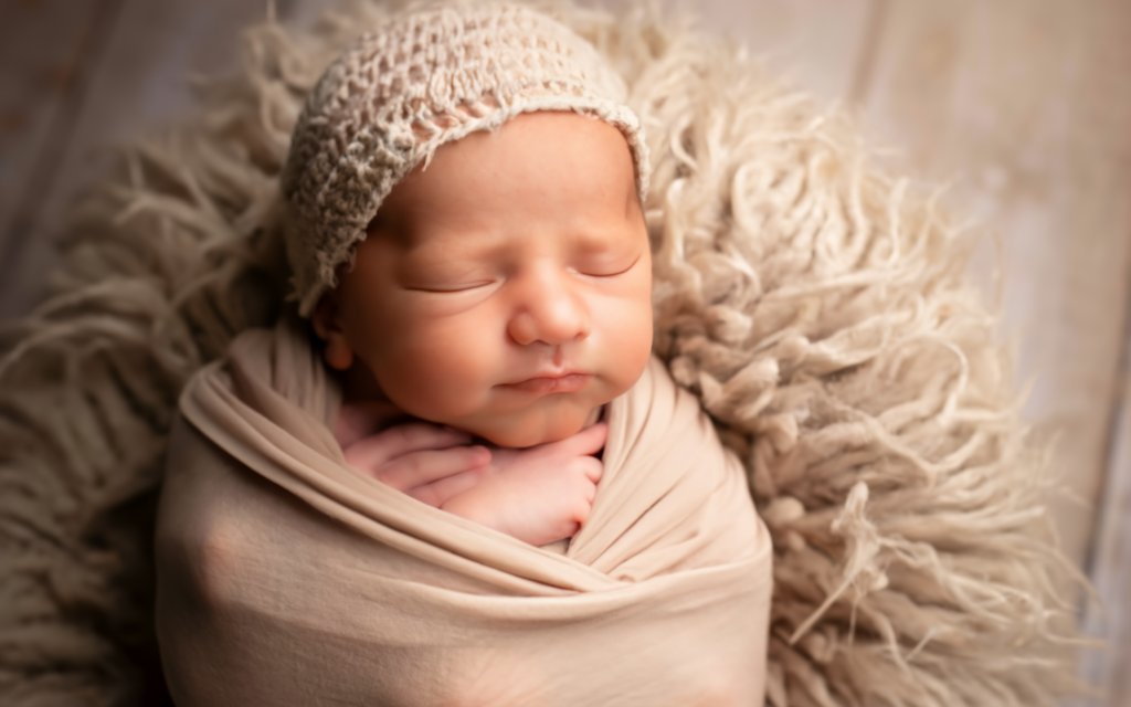 A close-up photo of a peaceful, sleeping newborn baby with a slightly Conehead, wrapped in a soft, cozy blanket. The background should be softly blurred, with pastel colors to evoke a sense of calm and reassurance. Include gentle light filtering from one side to highlight the baby’s features, creating a warm and comforting atmosphere. If possible, include a subtle graphic overlay or text that says 'Newborn Conehead: Causes, Concerns, and Comforting Facts' in a clean, modern font.